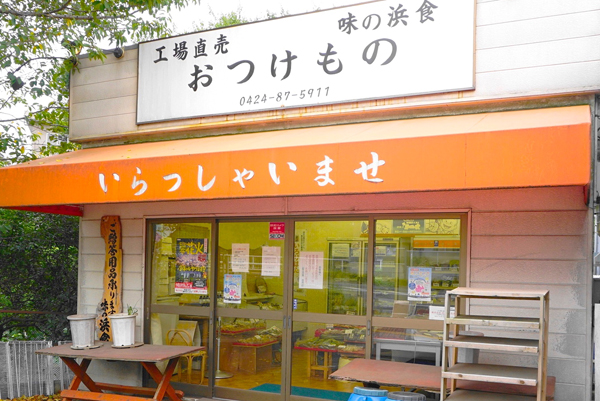 「いらっしゃいませ」と書かれたオレンジの軒先。看板には「工場直売　味の浜食　おつけもの」